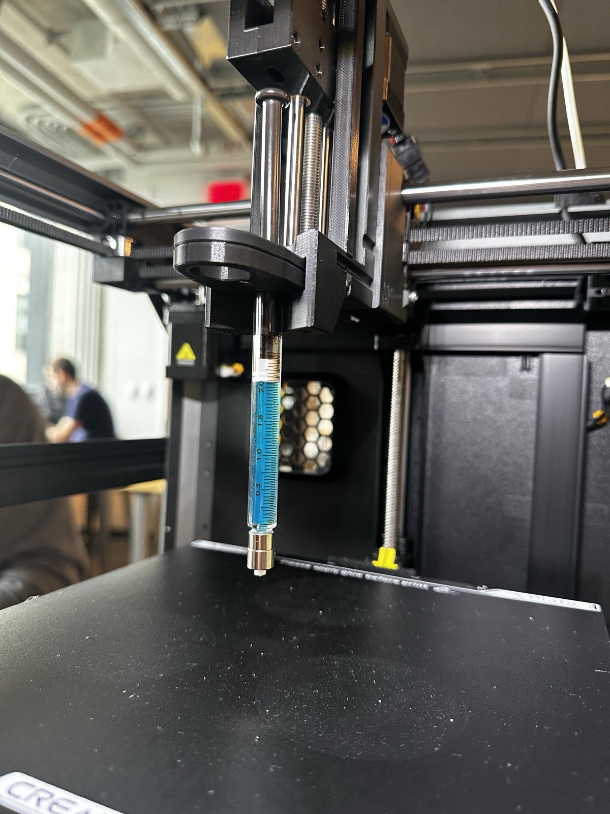 A syringe of blue bioink mounted in the syringe pump, above the printer bed