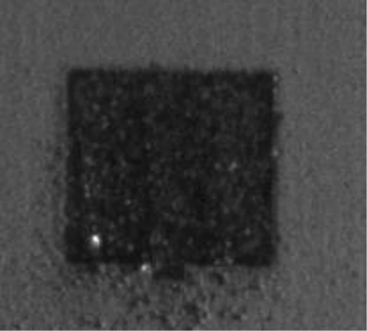 The powder bed before the powder was spread: a dark rectangular part footprint with two bright spots at its lower left.
